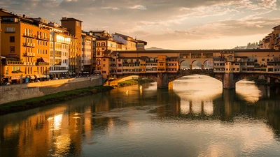 Ponte Vecchio in Florence at golden hour, medieval bridge over the Arno with overhanging shop houses and the Vasari Corridor running along the top