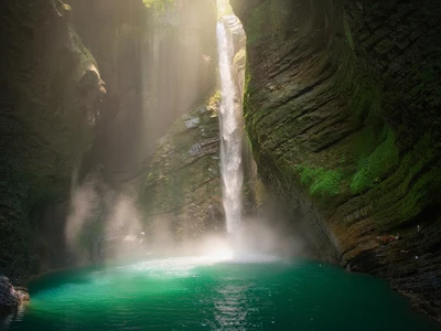 Slap Kozjak waterfall in Slovenia, 15-meter cascade into a circular emerald plunge pool inside a limestone amphitheater cave